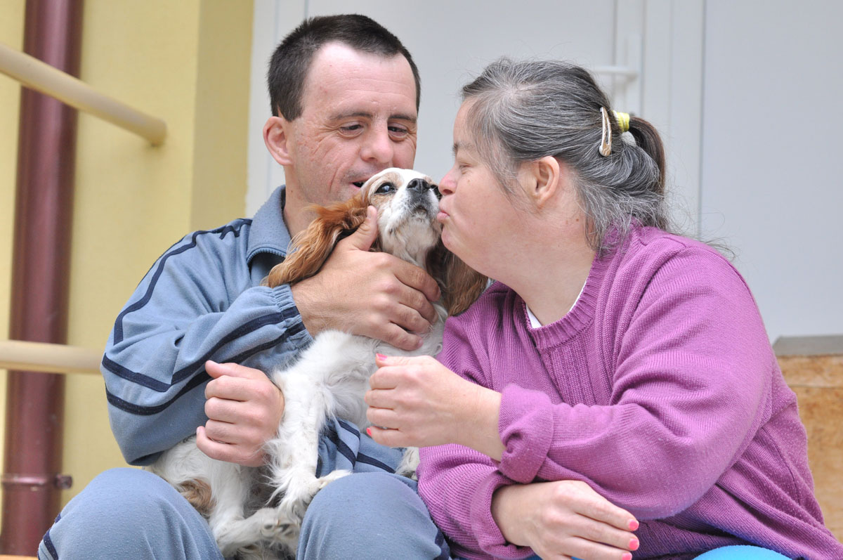 An aging couple with disabilities play with their dog. 