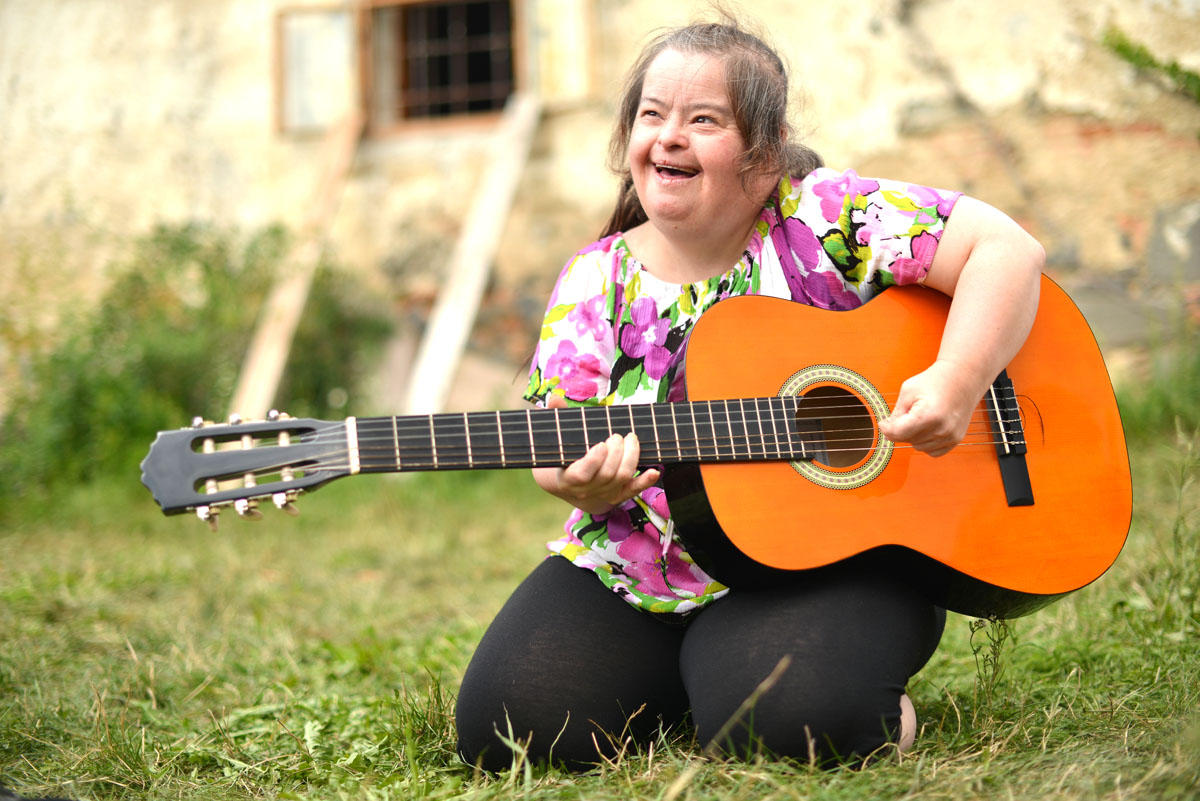 A person with disability plays a guitar outside.